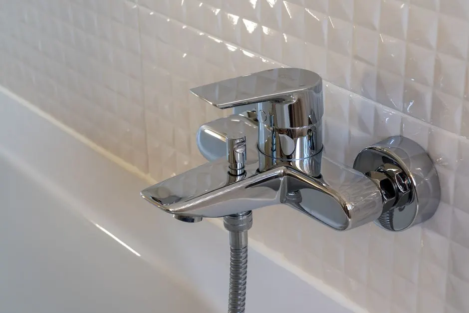 Close-up of a contemporary chrome faucet in a modern bathroom with white geometric tiles.